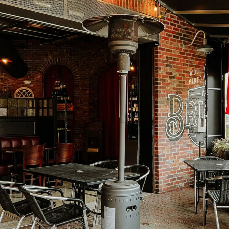 Industrial brick-walled restaurant patio with outdoor heaters, dark wood tables, leather booths, wicker chairs, and colorful hanging flags.