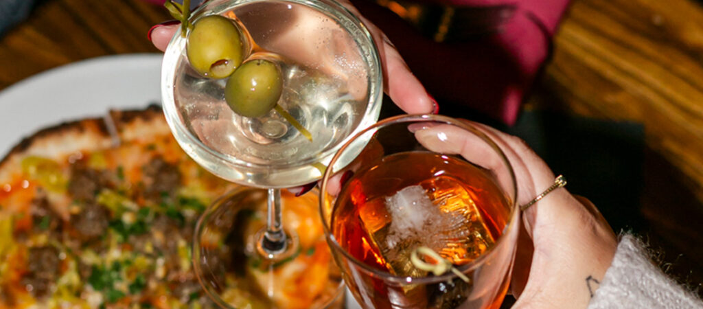 Toasting handcrafted cocktails and martini over pizza from The Bricks Pizzeria drink menu