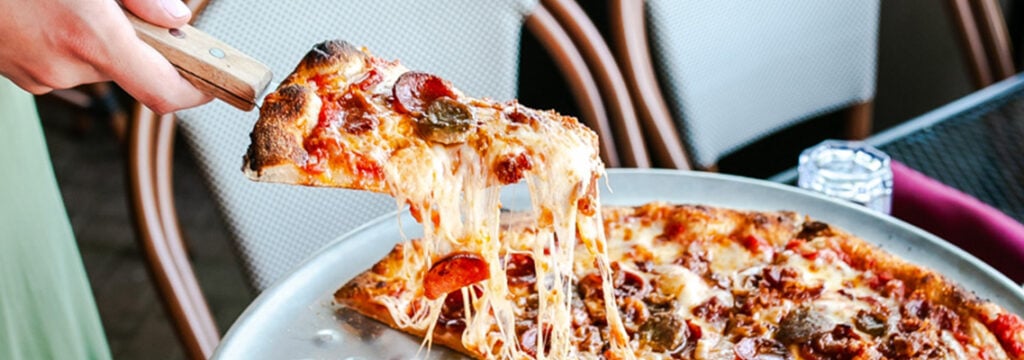 Freshly baked pizza slice with melted cheese pull from The Bricks Pizzeria food menu